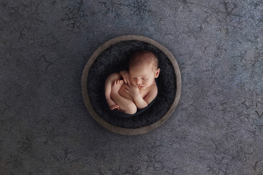 Newborn baby boy sleeping in a round bowl with dark fur, serene Essex portrait session